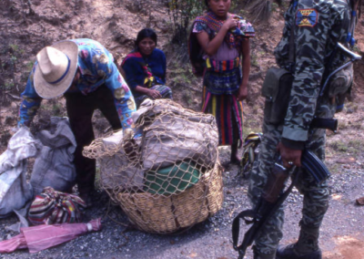 A soldier inspecting a Mayan man's basket in search of subversive materials