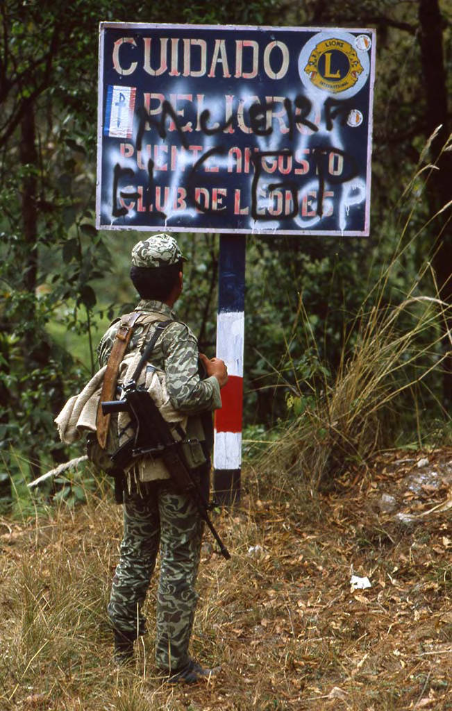 Armed soldier looks at anti-guerrilla slogans on a street sign